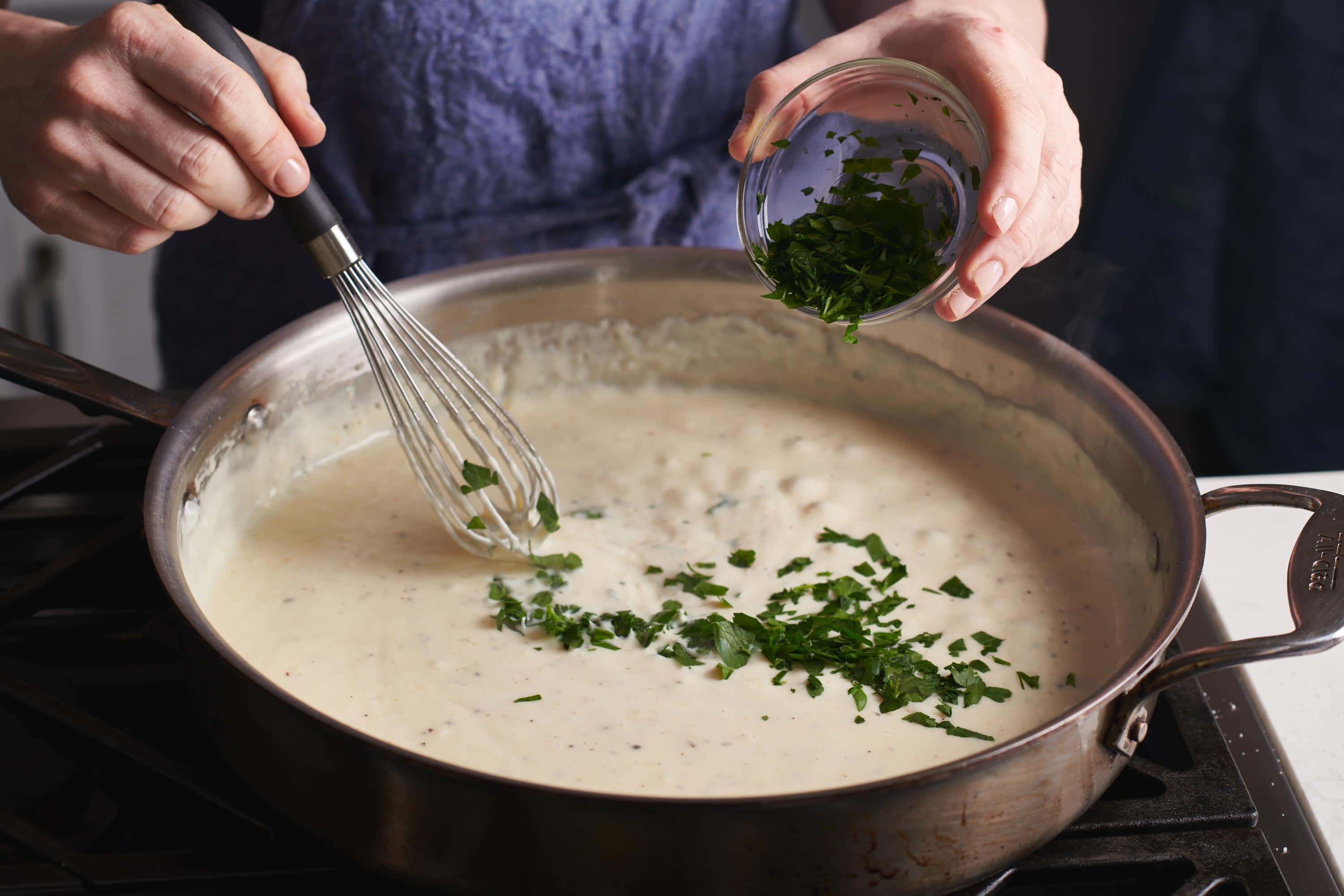 Woman sprinkling parsley into a skillet of Alfredo.