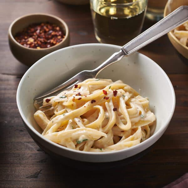 Easy Creamy Fettuccine Alfredo in bowl with red pepper flakes on table.