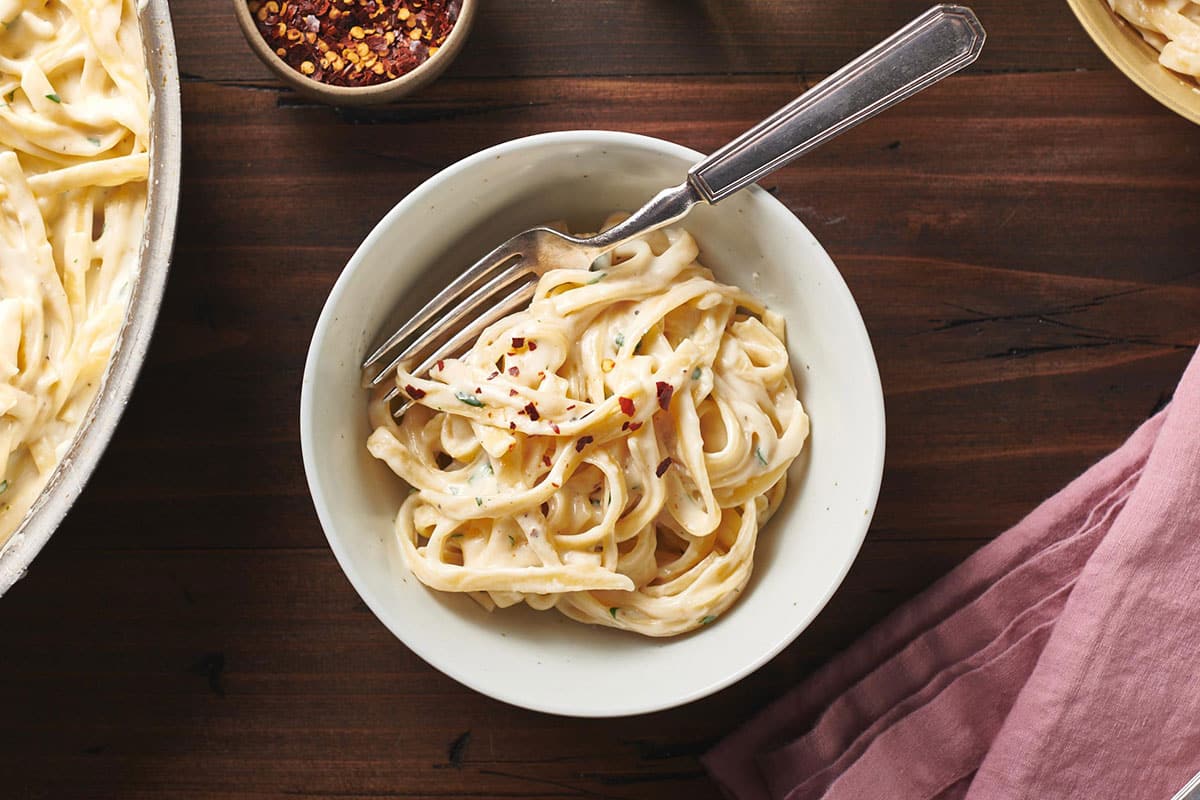 Creamy Fettuccine Alfredo in bowl with red pepper flakes on table.