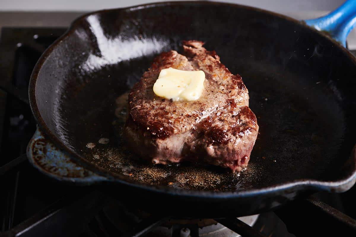 Filet Mignon in a skillet topped with a pat of butter.