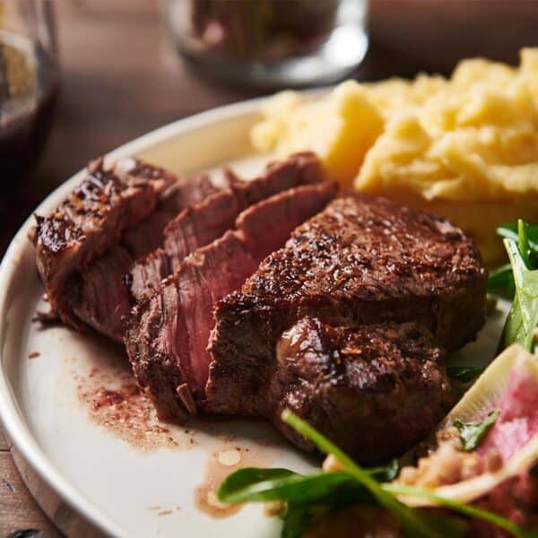 Filet mignon on a white plate with potatoes and salad on the side.
