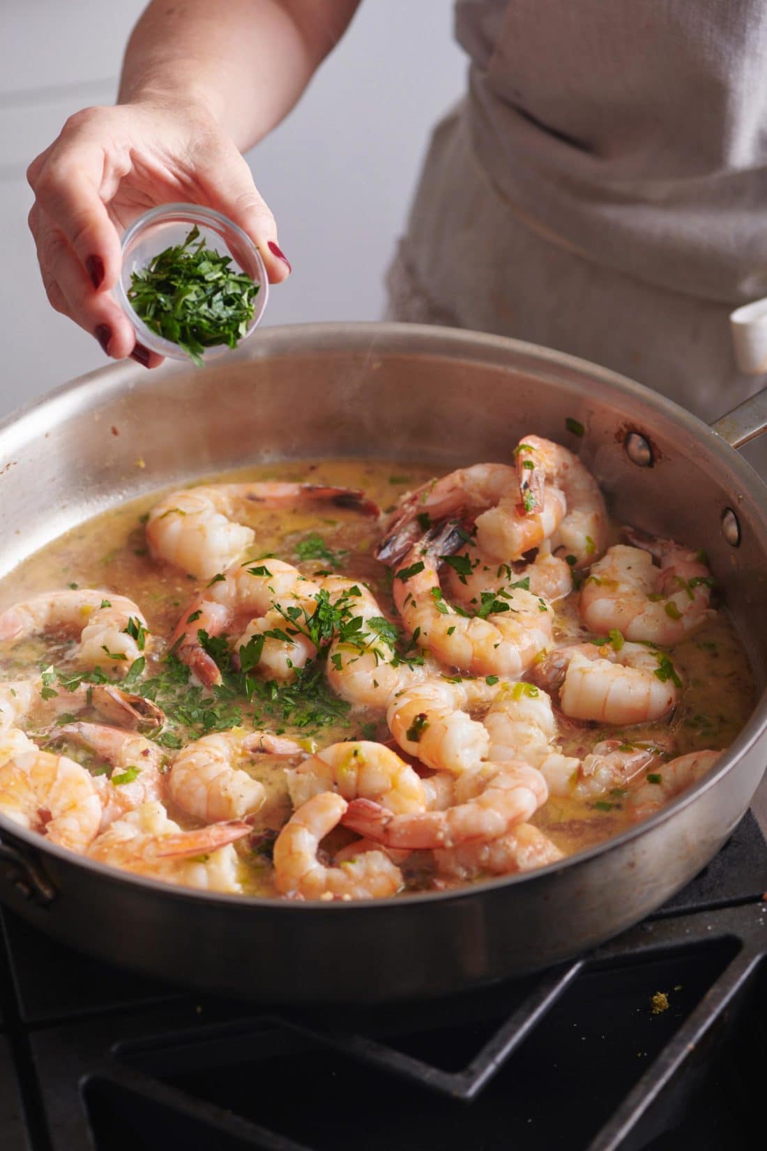 Woman sprinkling parsley into a skillet of shrimp.