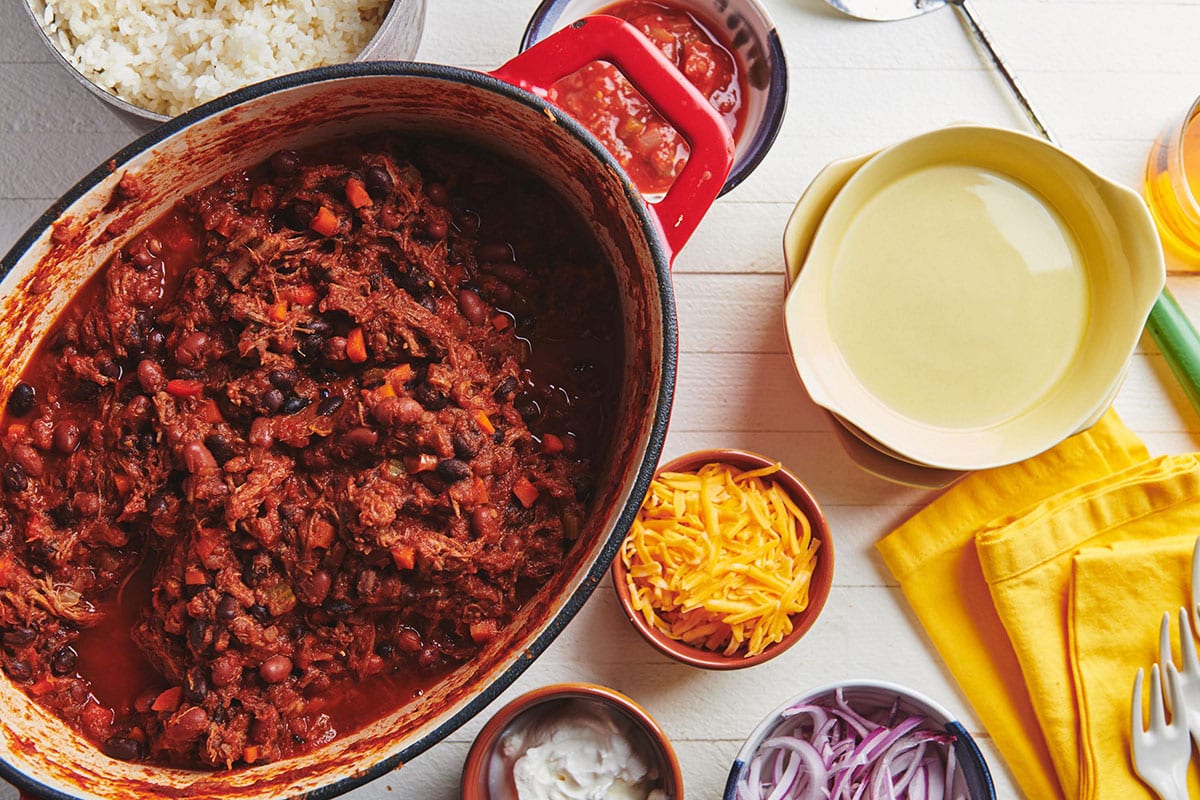 Barbacoa Beef Chili in pot on table with toppings in bowls.