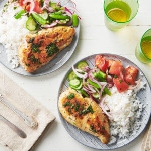 Plates of Cilantro Lime Chicken, rice, salad, and tomatoes on a white, wooden table.