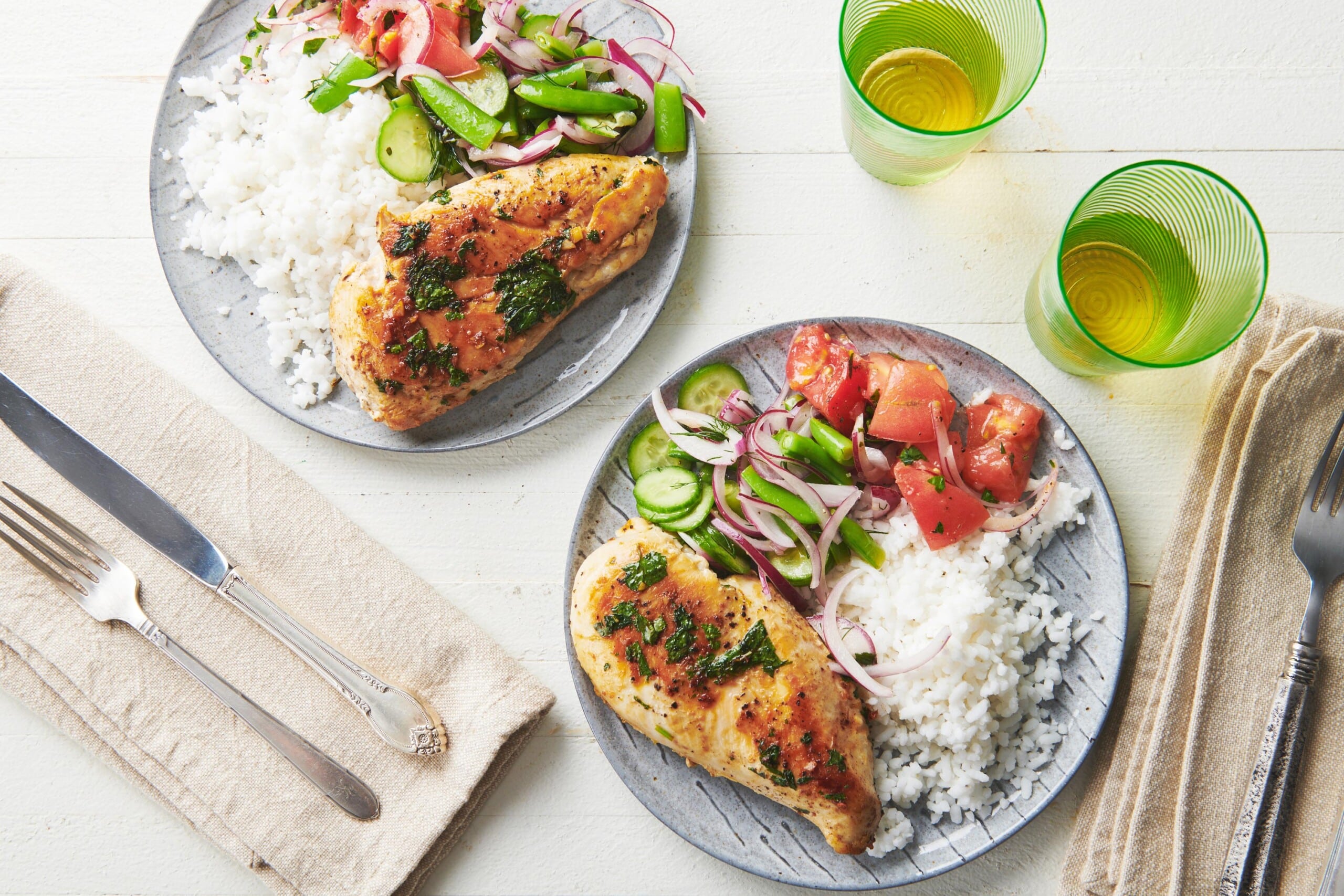 Plates of Cilantro Lime Chicken, rice, salad, and tomatoes on a white, wooden table.