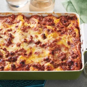Classic meat lasagna in green and white baking dish on table.