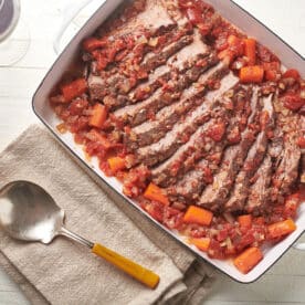 Jewish-style brisket in white dish on table with serving spoon.