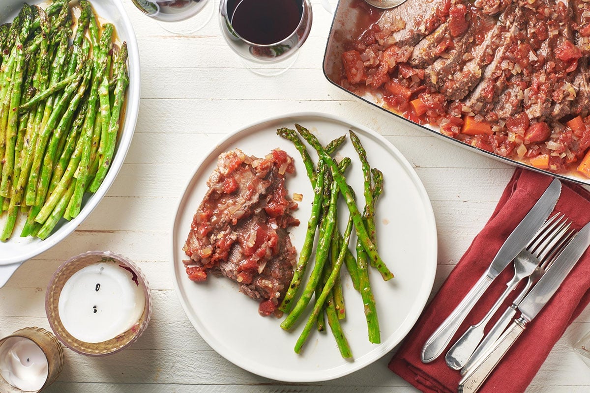 Brisket in tomato-based sauce on plate with roasted asparagus.