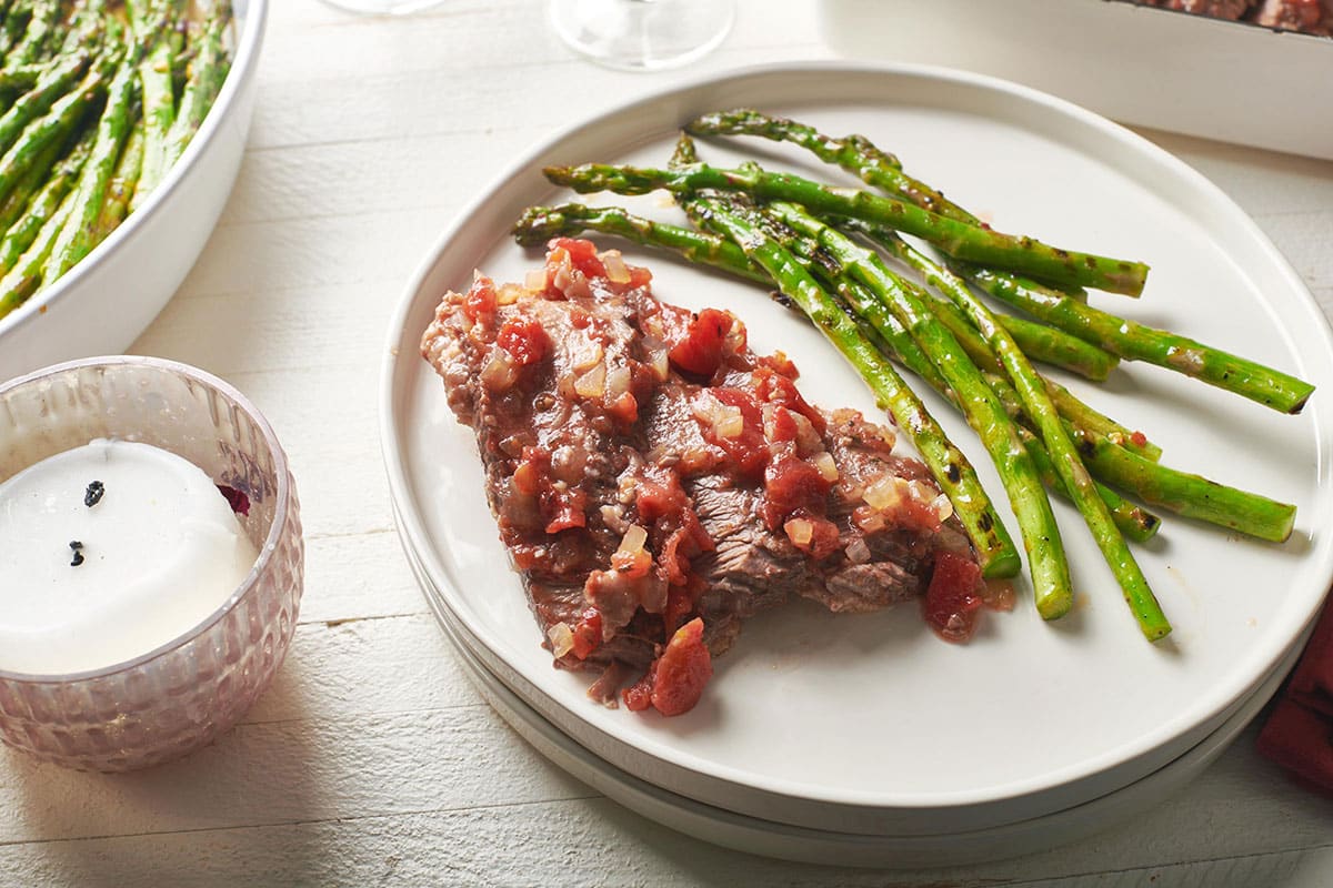 Brisket in tomato sauce on plate with cooked asparagus.