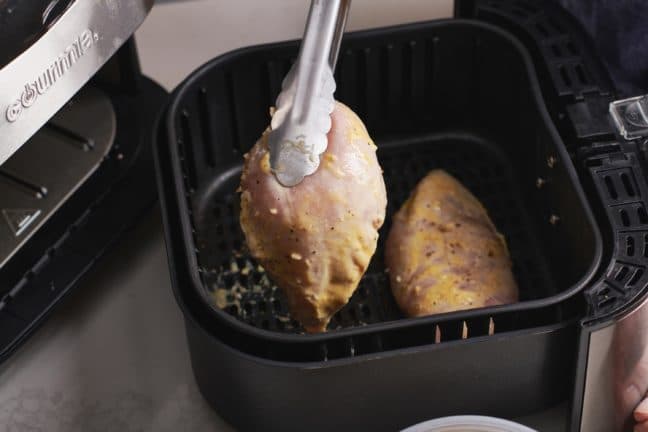 Tongs placing Chicken Breasts into an Air Fryer.