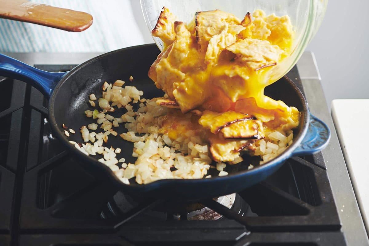 Pouring matzoh and eggs into pan of onions for Matzoh Brei.