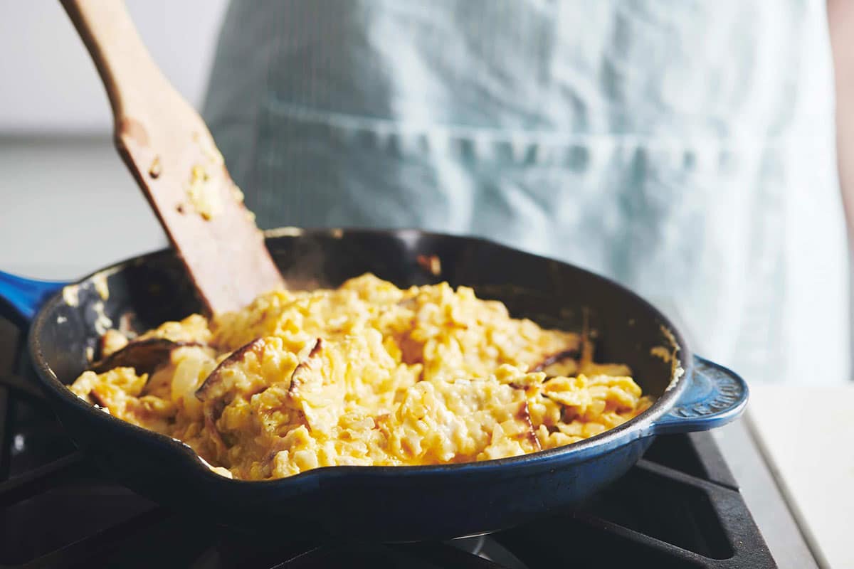 Stirring matzoh brei in pan on stove with wood spoon.