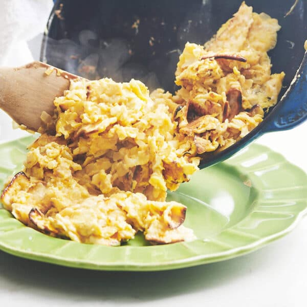 Wooden spatula pushing Matzoh Brei from a skillet to a plate.