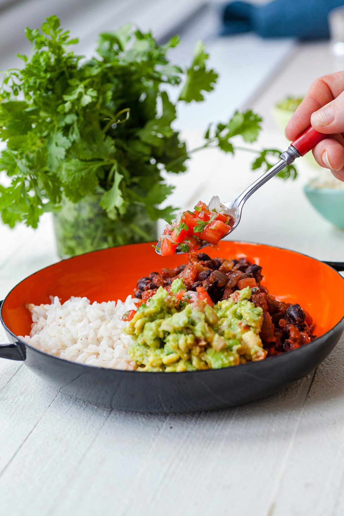 Spoon adding salsa to a bowl with guacamole, Black Beans, and Rice.