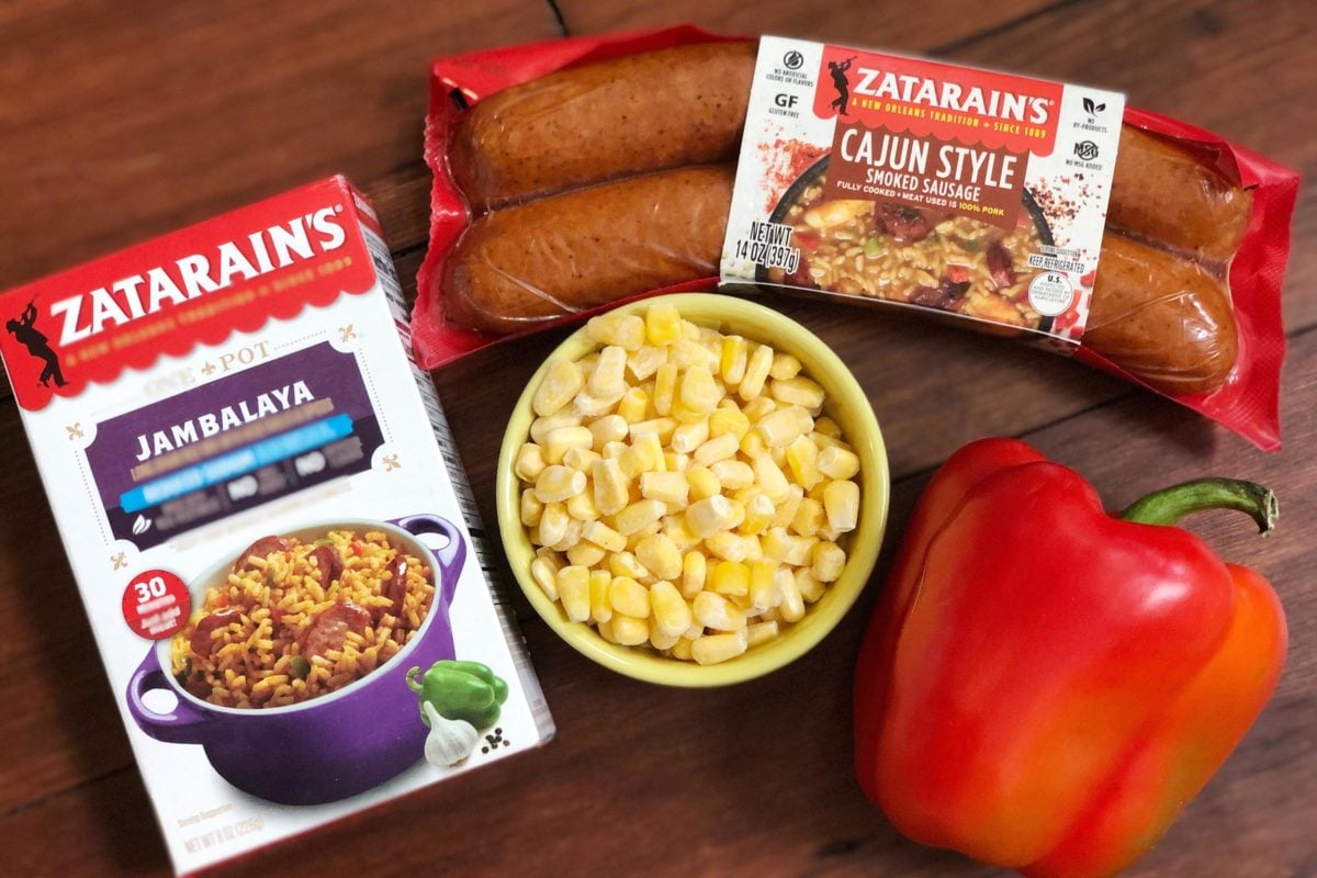 Zatarain\'s Cajun sausage, Zatarain\'s Jambalaya, corn, and a red pepper on a wooden table.