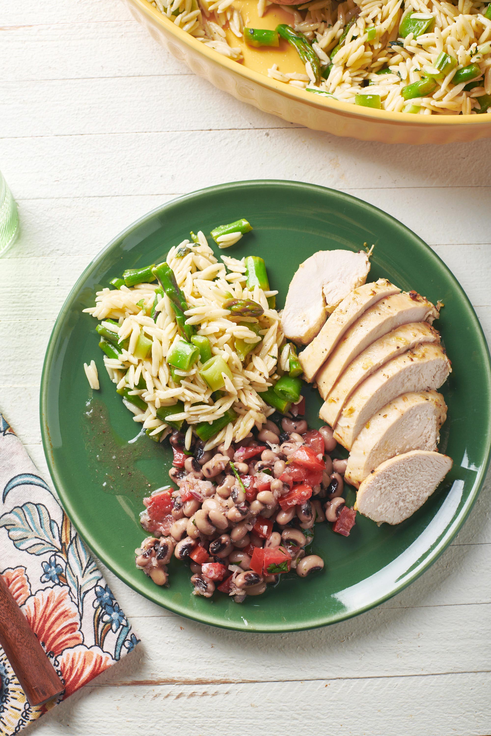 Herb Orzo Salad on a plate with sliced chicken and black eye pea salad