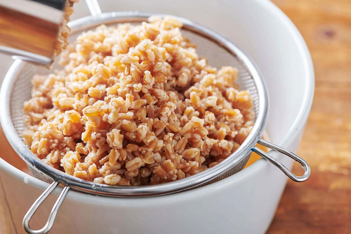 Cooked farro in strainer over white bowl.