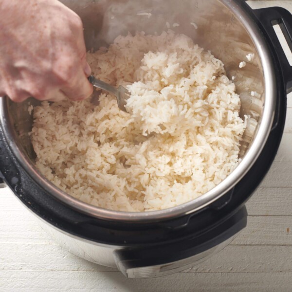 Woman using a fork to fluff steaming rice in an Instant Pot.
