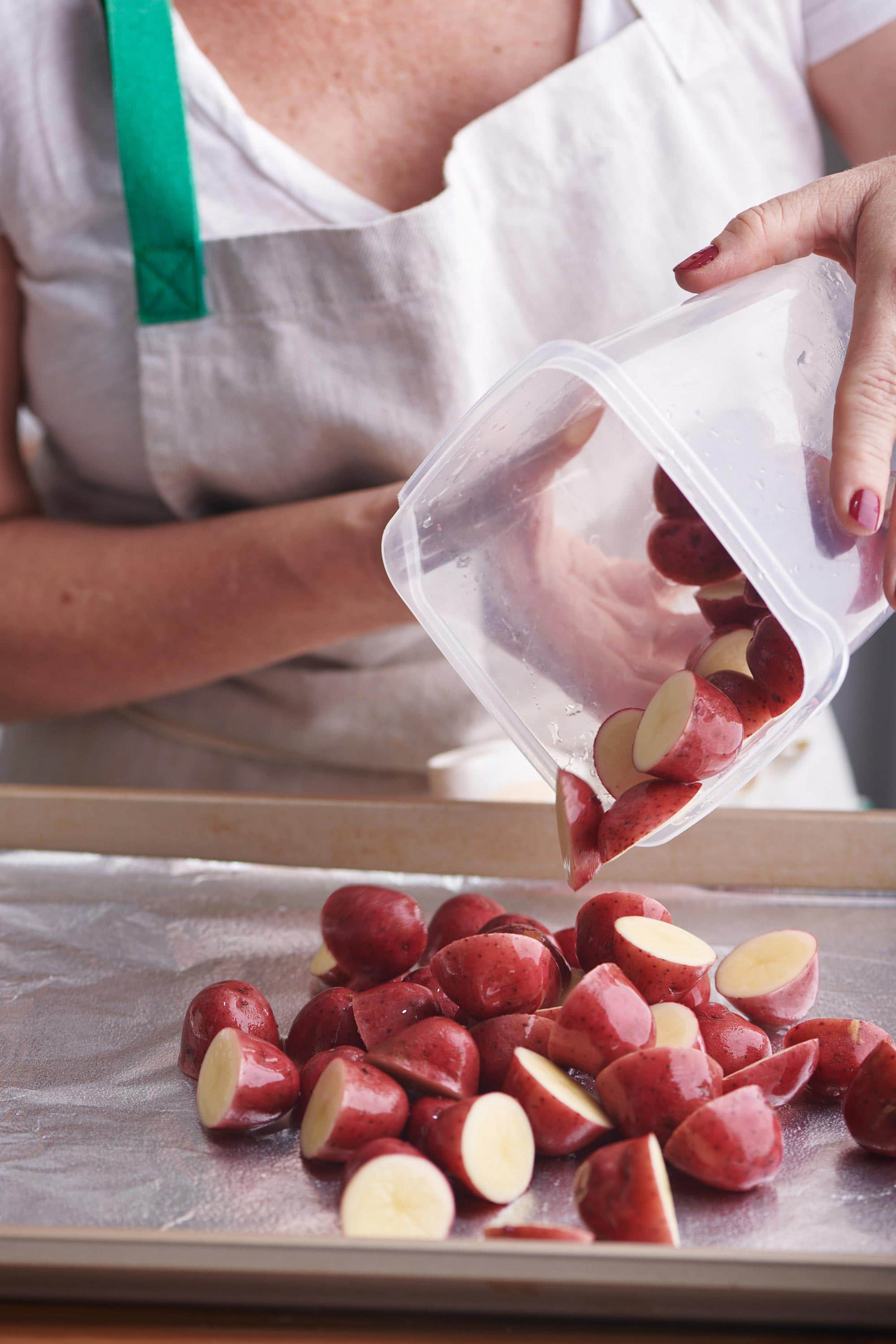 Woman pouring halved red potatoes onto a foil lined baking sheet.