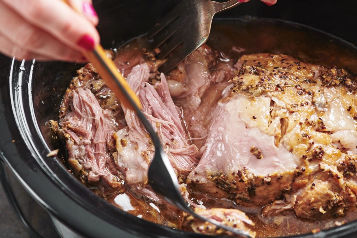 Forks shredding Pork Butt with Brown Sugar, Garlic and Herbs in a Crock Pot.