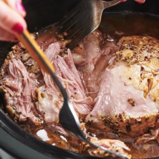 Forks shredding Pork Butt with Brown Sugar, Garlic and Herbs in a Crock Pot.