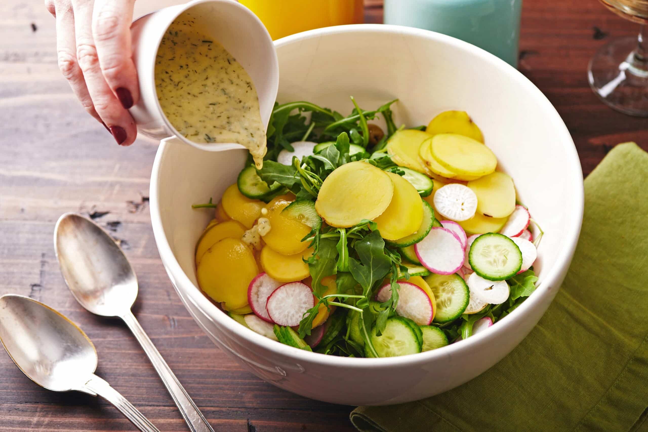 Pouring Tzatziki Vinaigrette over Arugula and Cucumber Salad.