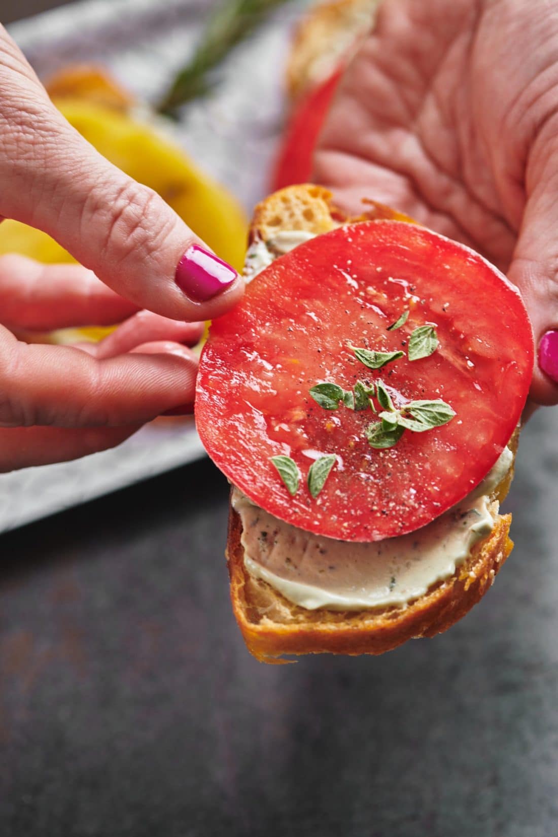 Woman placing a red tomato slice on bread with herbed whipped ricotta.