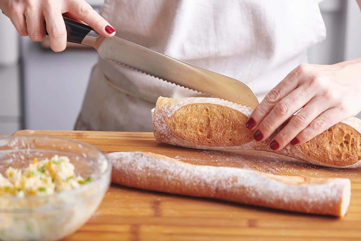 Woman slicing a baguette horizontally.