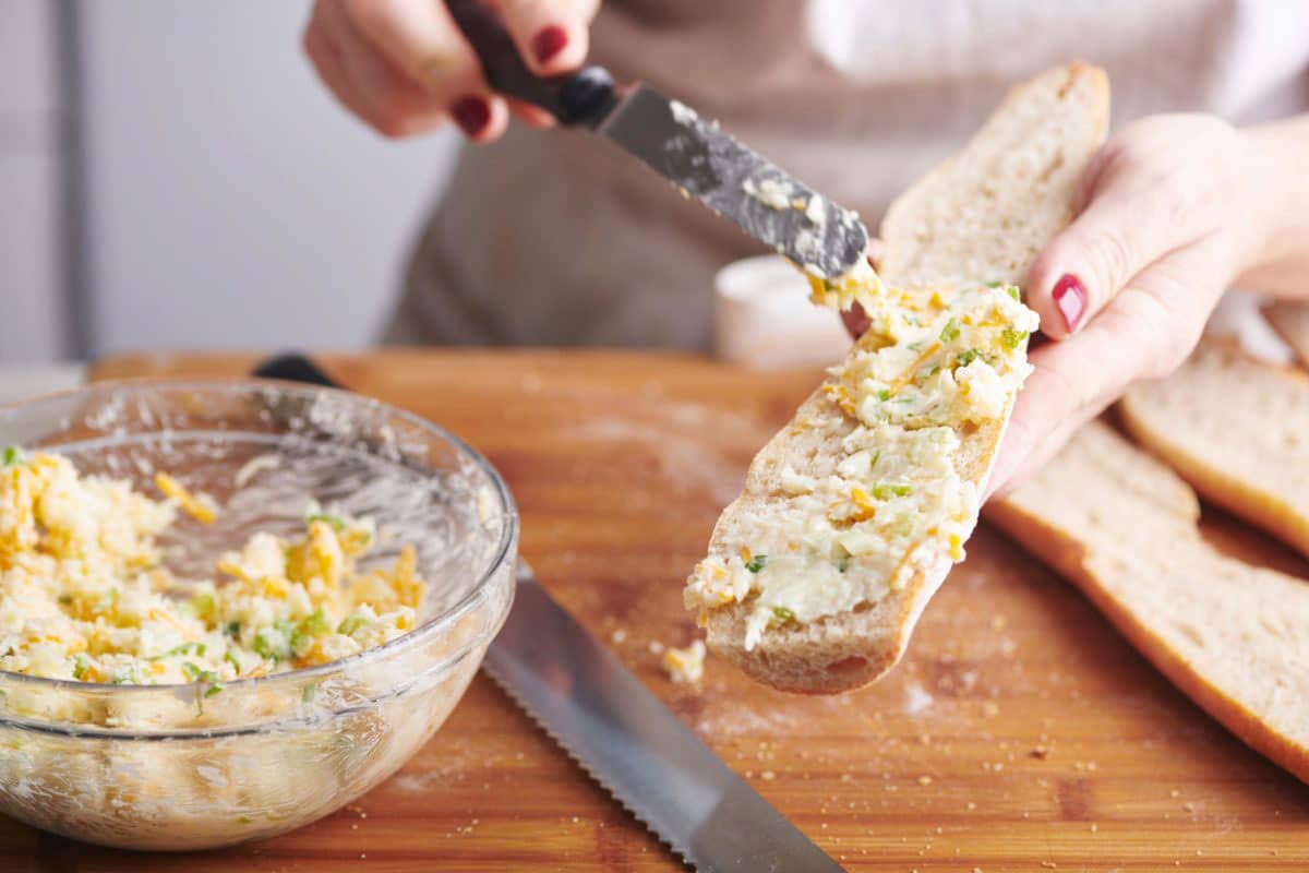 Woman spreading a cheese and butter mixture onto sliced baguette.