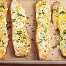 Four slices of cheese garlic bread on parchment-lined baking sheet.