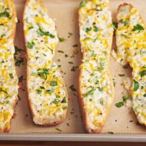 Four slices of cheese garlic bread on parchment-lined baking sheet.