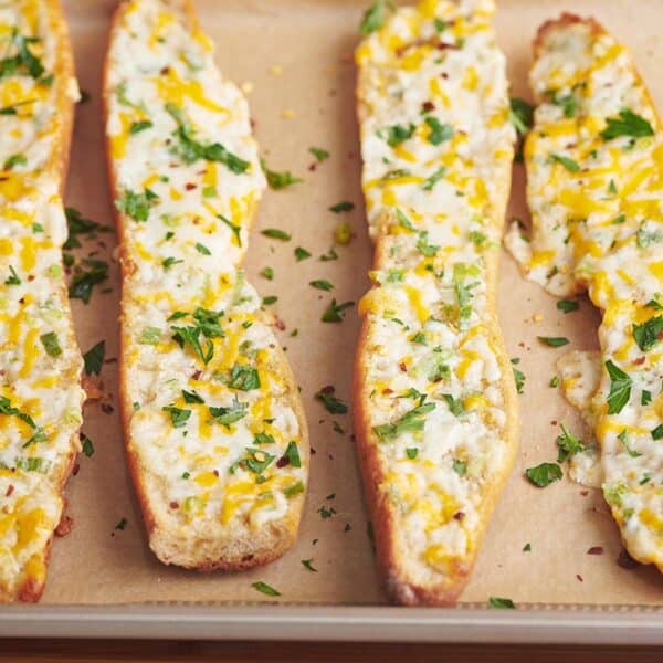 Four slices of cheese garlic bread on parchment-lined baking sheet.