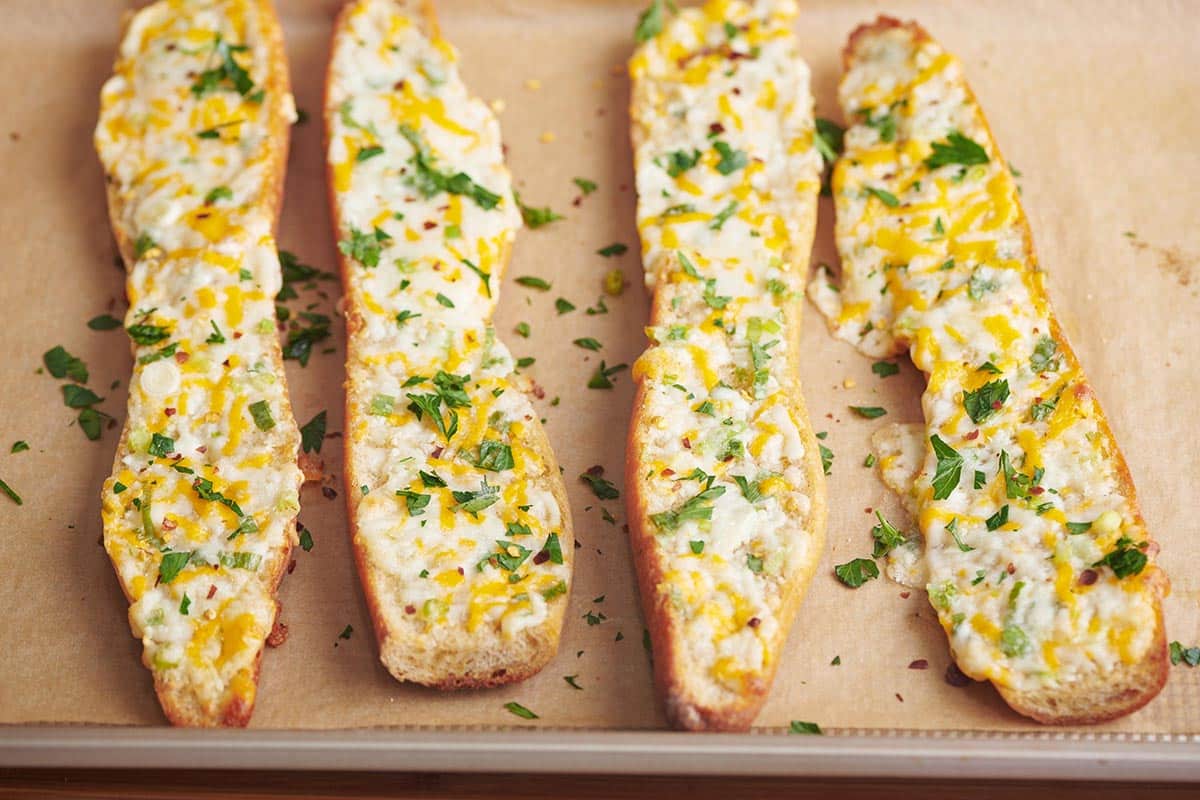 Four slices of cheese garlic bread on parchment-lined baking sheet.
