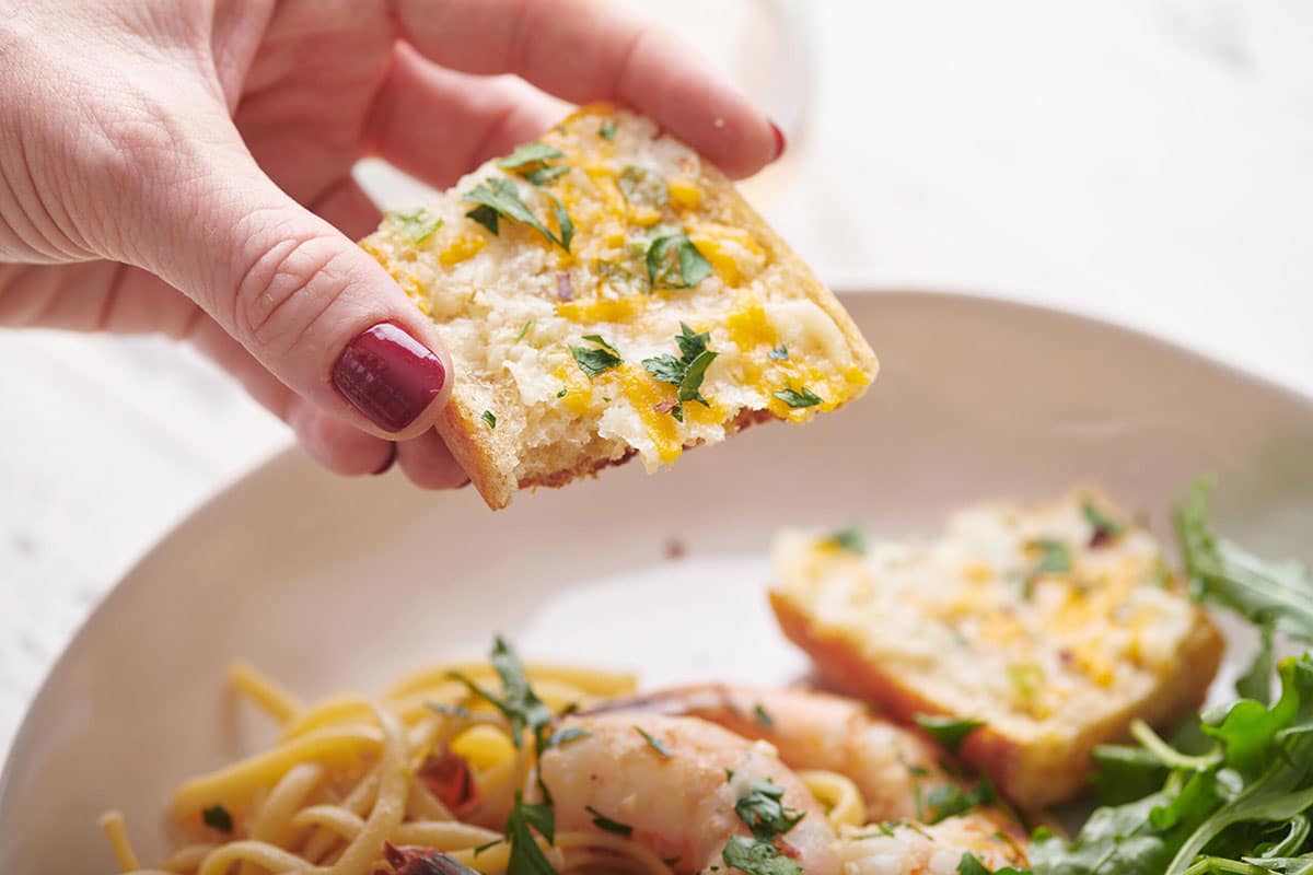 Woman holding a slice of Cheesy Garlic Bread.