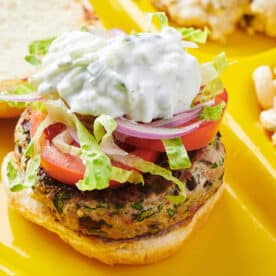 Greek turkey burger with tzatziki, lettuce, tomato, and onion on plate with sides.
