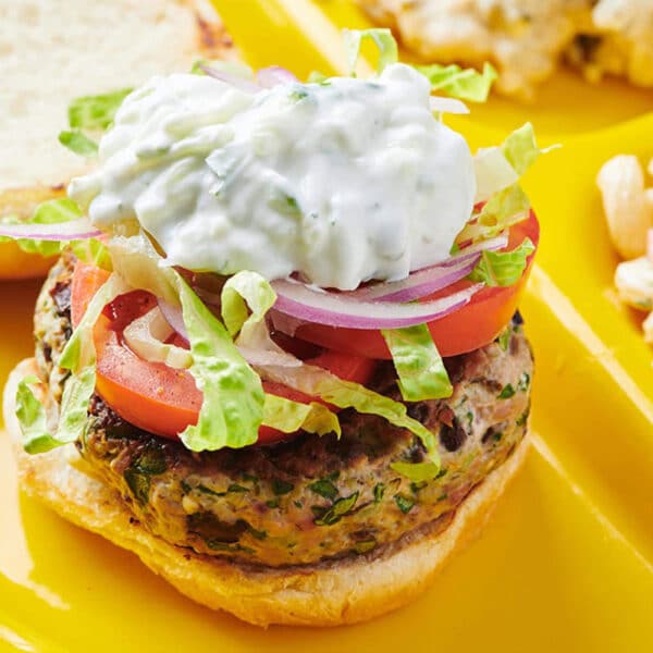 Greek turkey burger with tzatziki, lettuce, tomato, and onion on plate with sides.