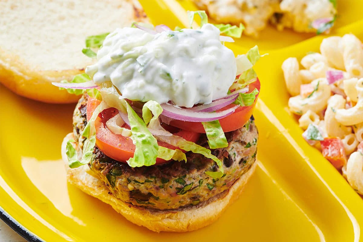 Greek turkey burger with tzatziki, lettuce, tomato, and onion on plate with sides.