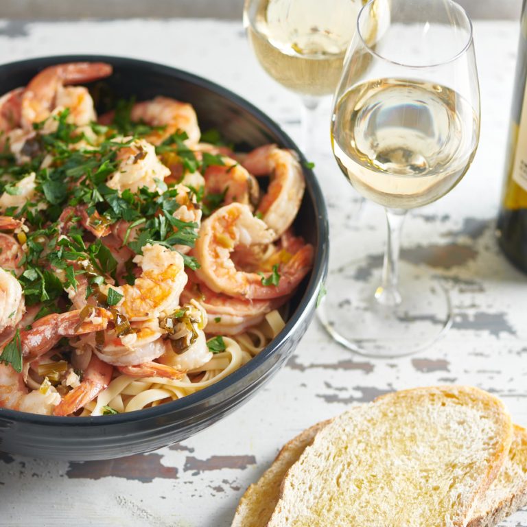 Glasses of white wine on a table with a bowl of Shrimp Scampi.