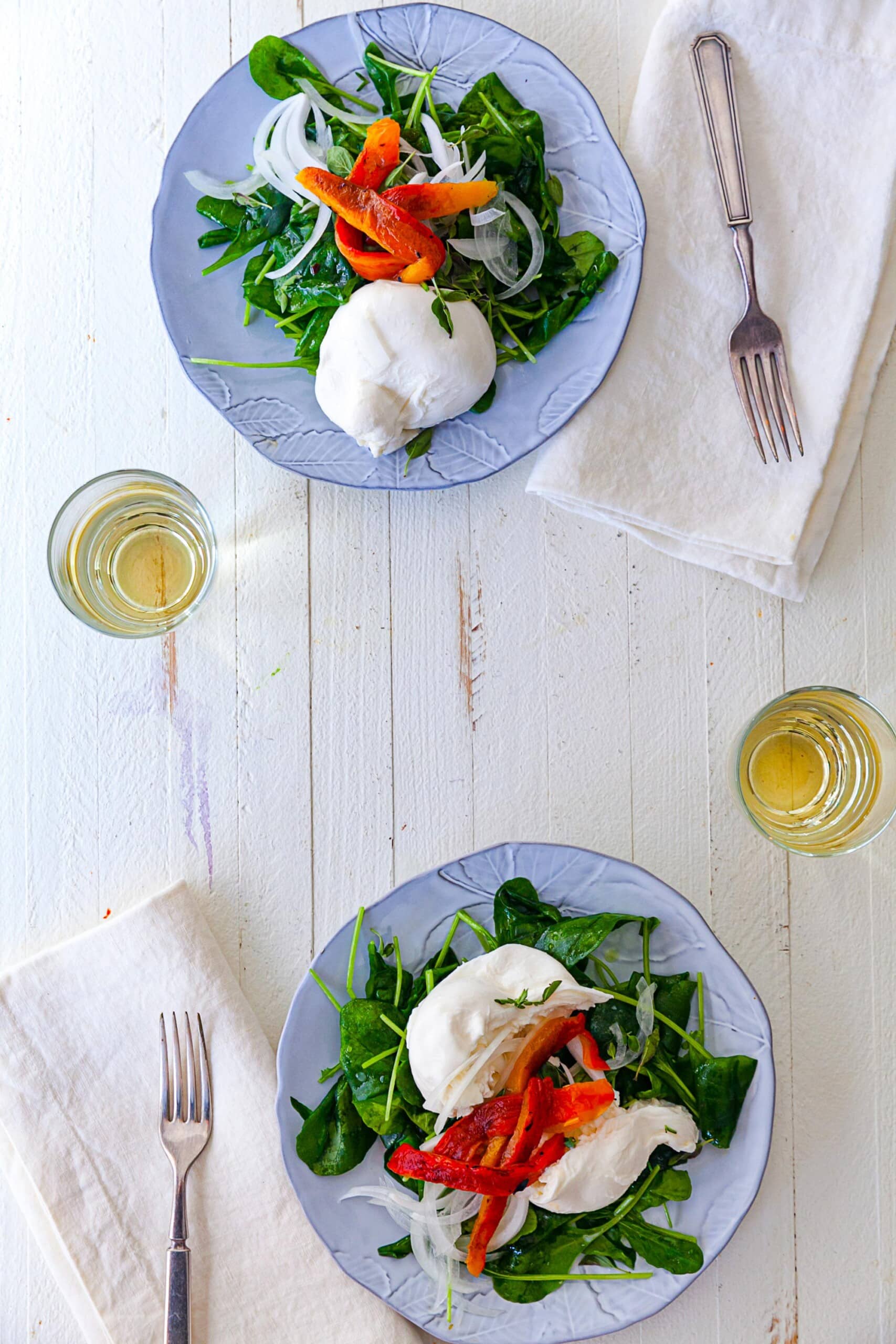 Spinach Salad topped with Burrata and roasted peppers on plates.