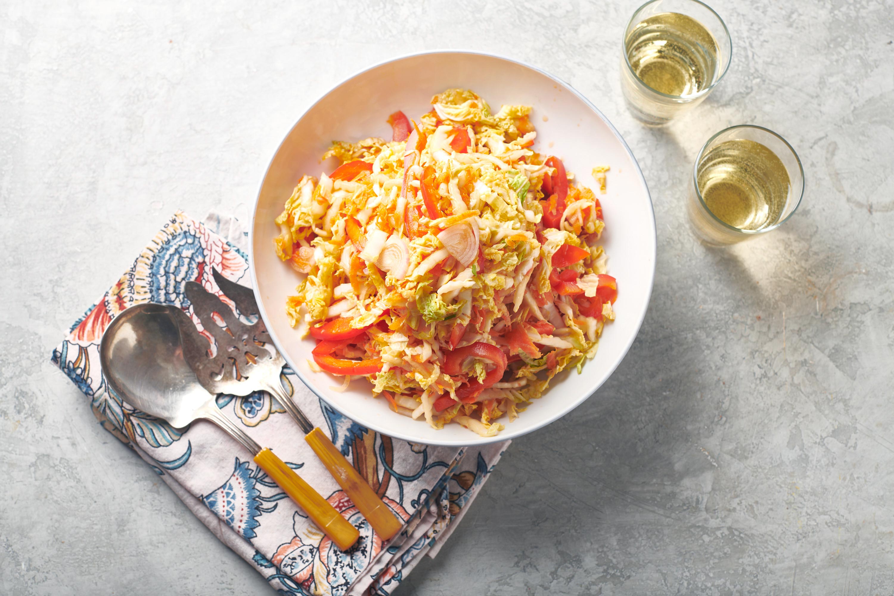 Vegan Asian Napa Cabbage Slaw in a white bowl next to silverware and glasses.