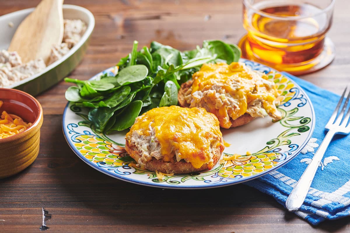 Open-faced tuna melt on colorful plate with side salad.