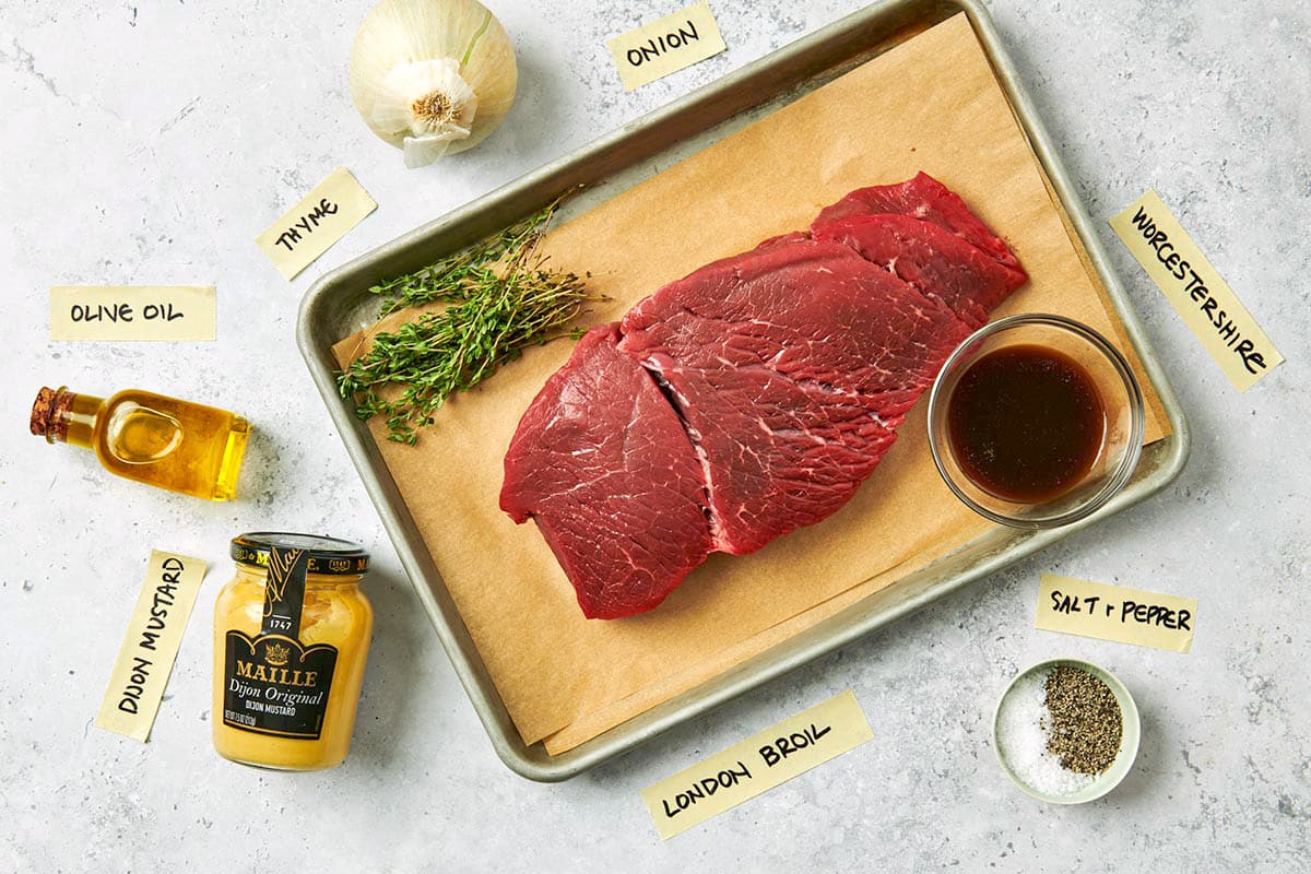 London broil, garlic, mustard, and other ingredients on marble table.