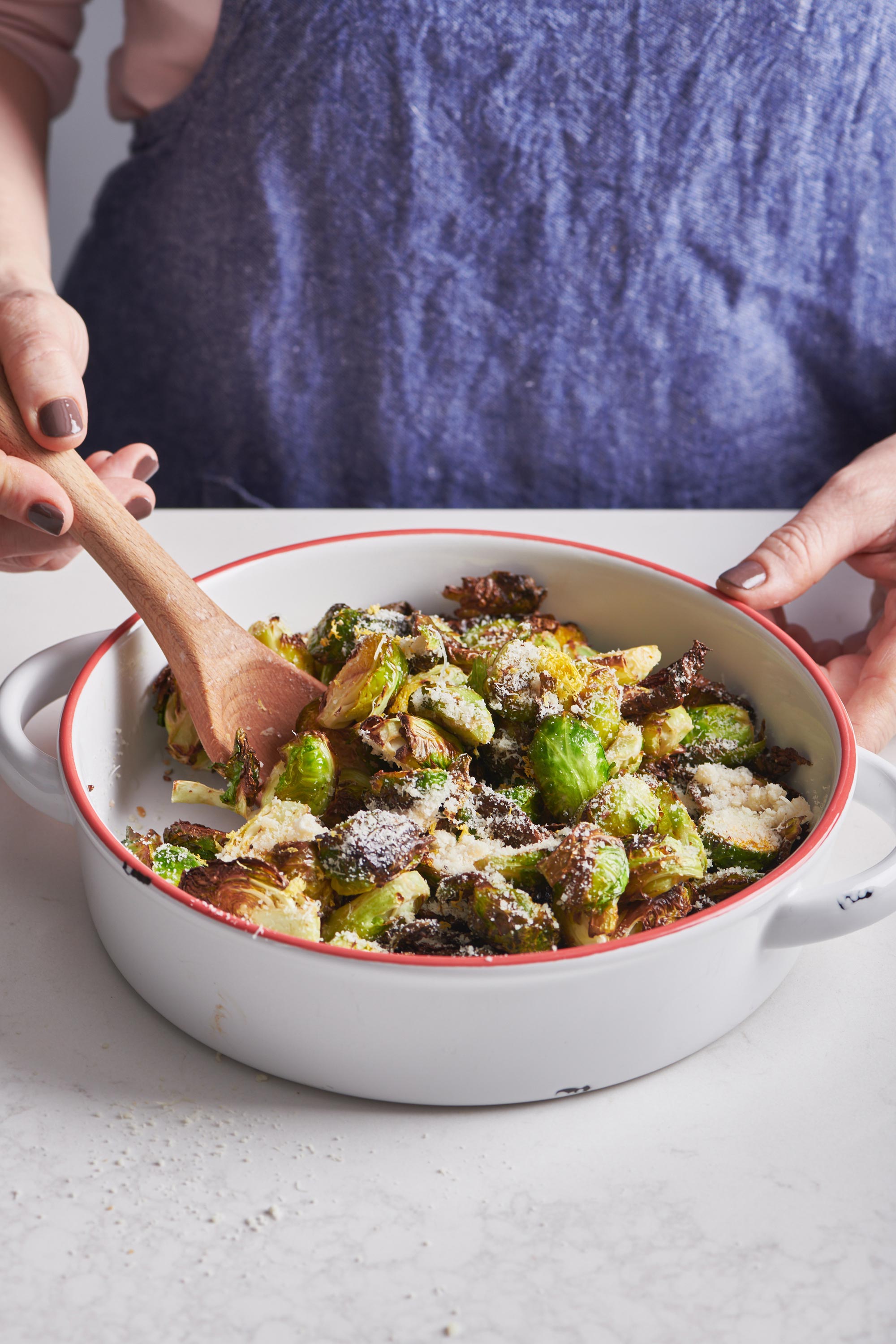 Woman stirring air-fried Brussels sprouts in bowl with a wooden spoon.