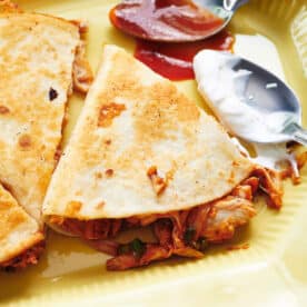 BBQ chicken quesadillas on plate with spoons of barbecue sauce and sour cream.