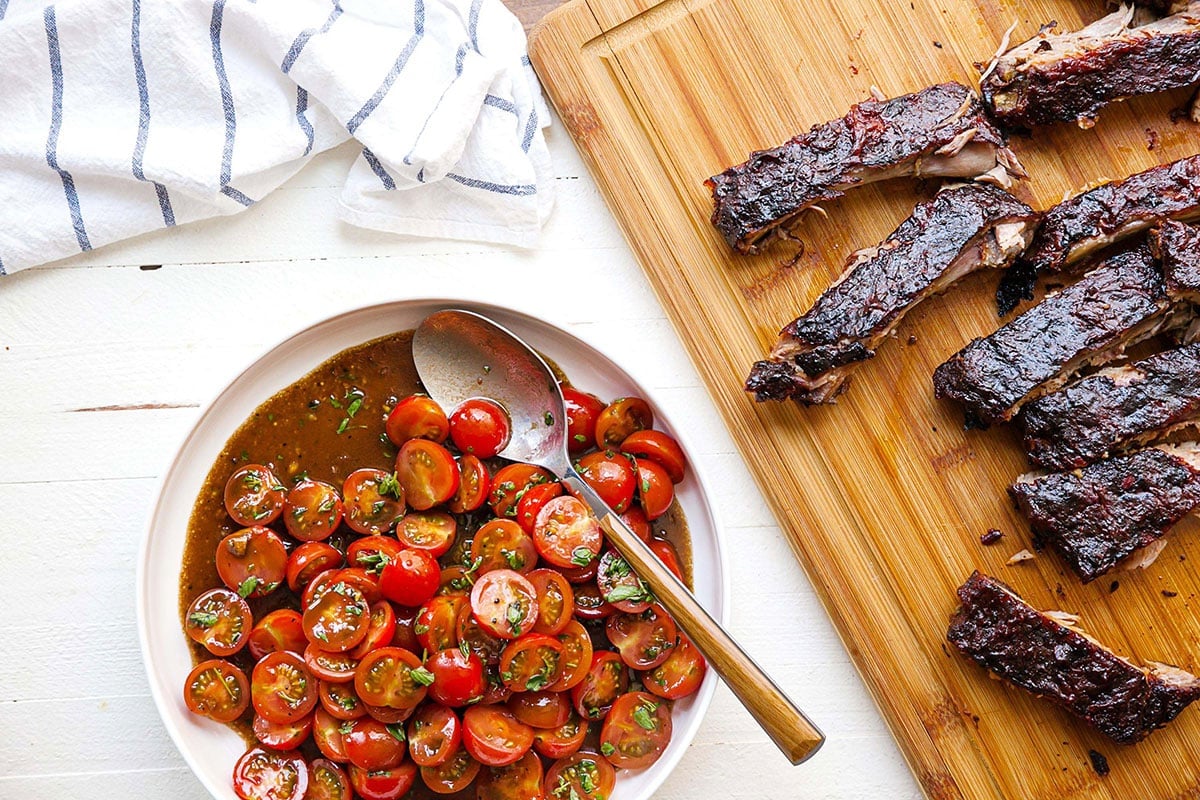 Cherry Tomato Salad next to cutting board with grilled ribs.