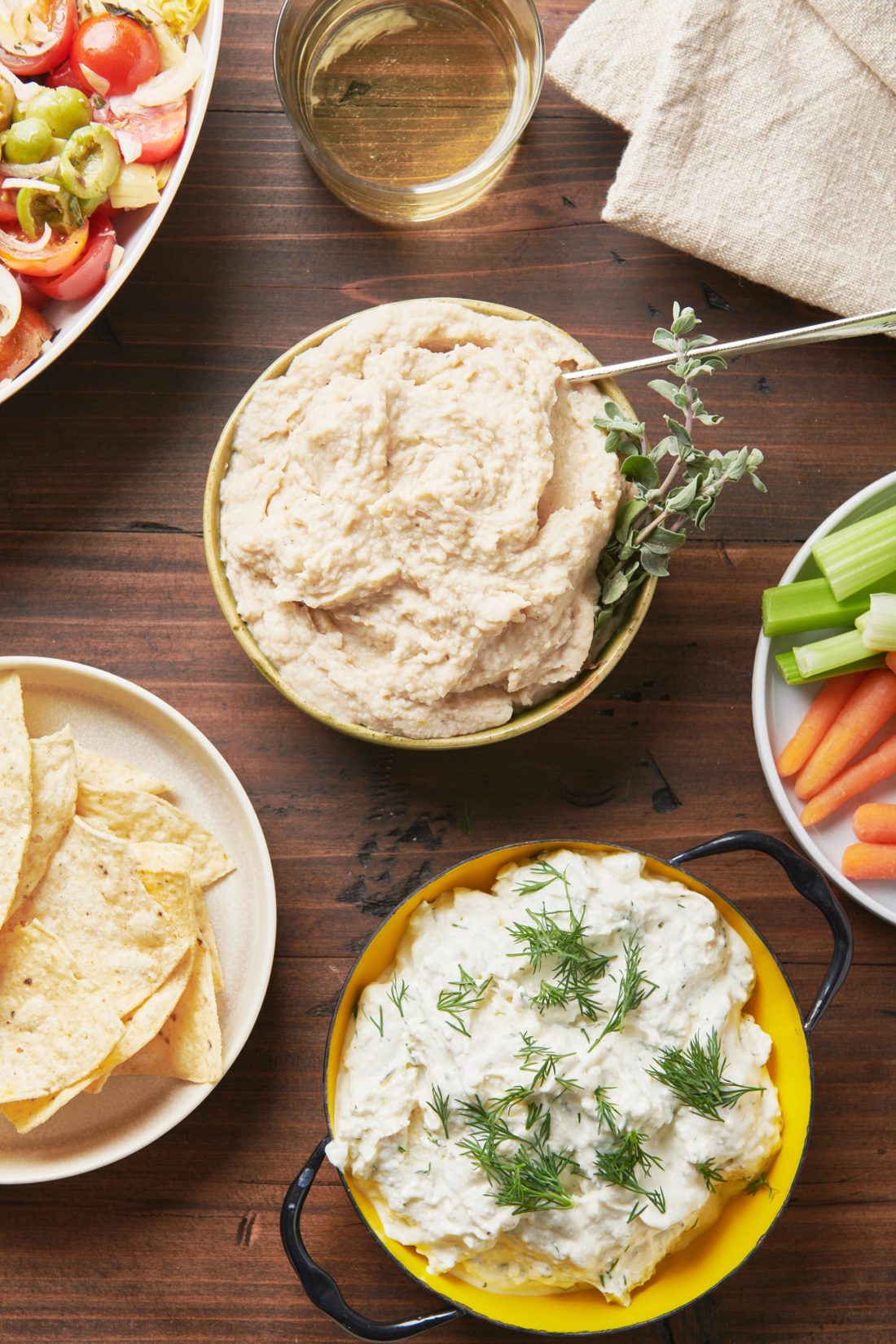 Bowls of Feta Yogurt Dip and hummus on a table with vegetables and chips.