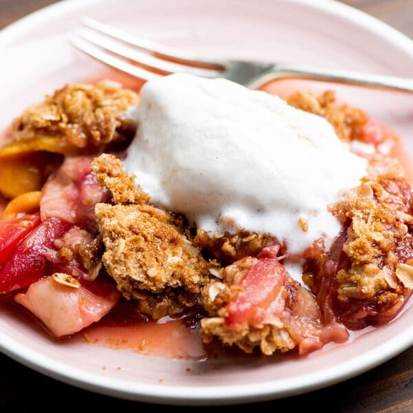 Plum and Nectarine Crisp with whipped cream on plate with fork.