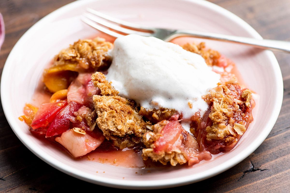 Plum and Nectarine Crisp with whipped cream on plate with fork.