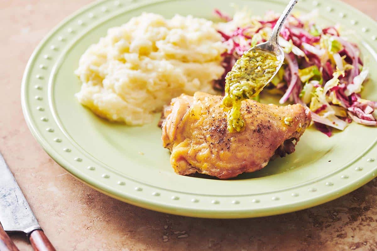 Roasted Chicken Thighs with green olive sauce being spooned over.