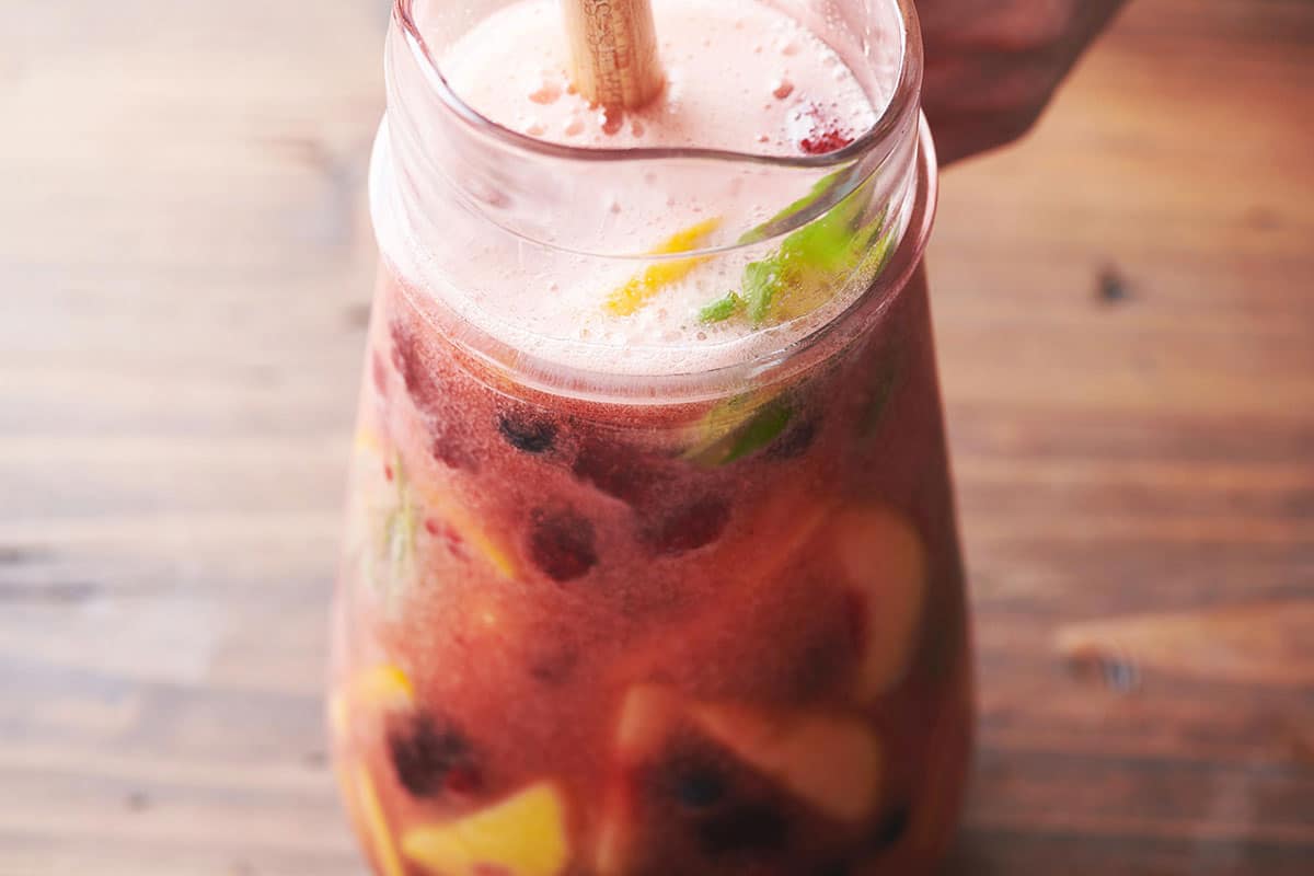 Stirring pitcher of sangria filled with summer fruits.